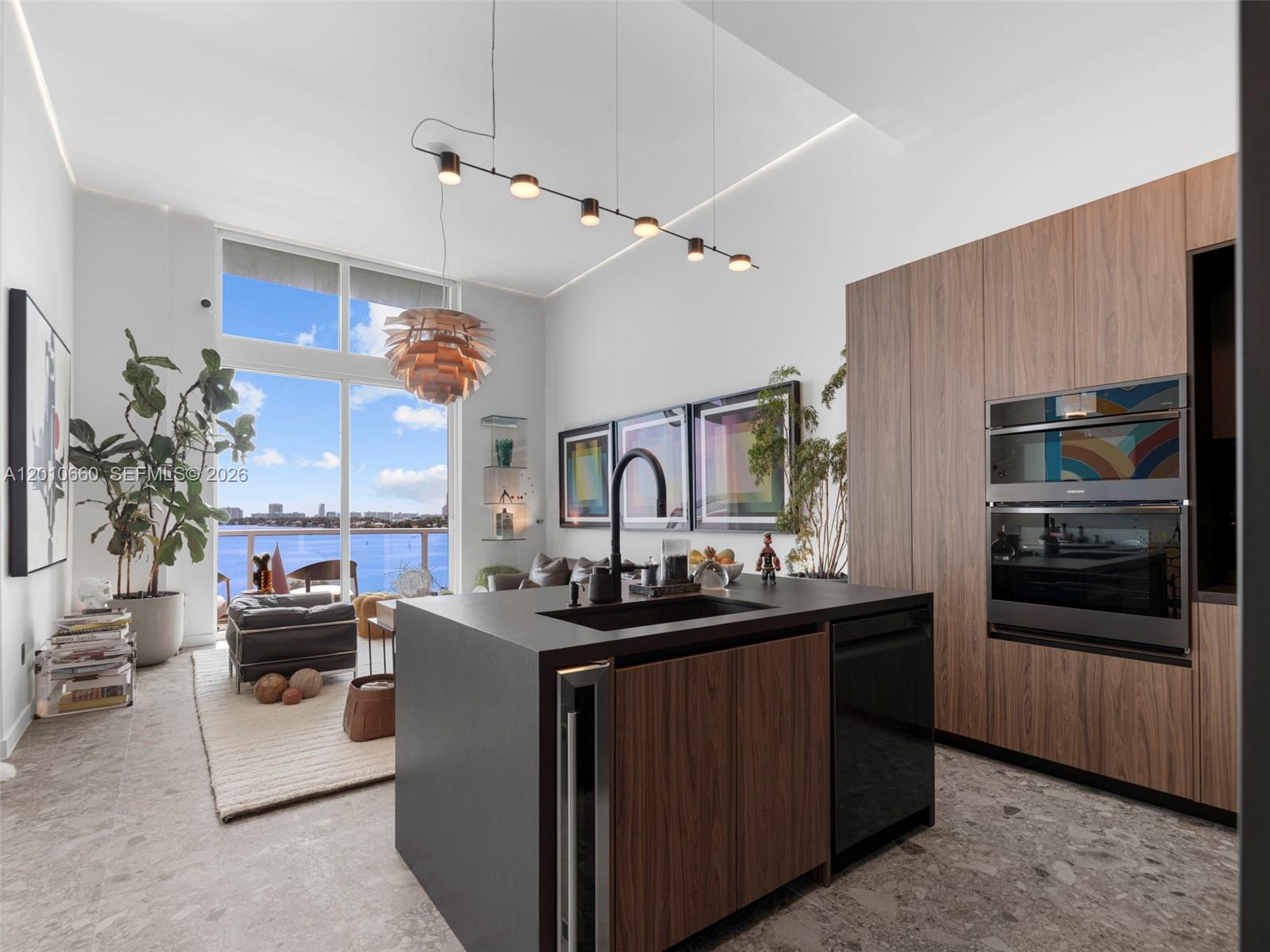 A modern kitchen with wood cabinetry and a dark island overlooks a balcony and water — 1900 N Bayshore Dr # 903, Miami FL 33132, MIAMI, FL