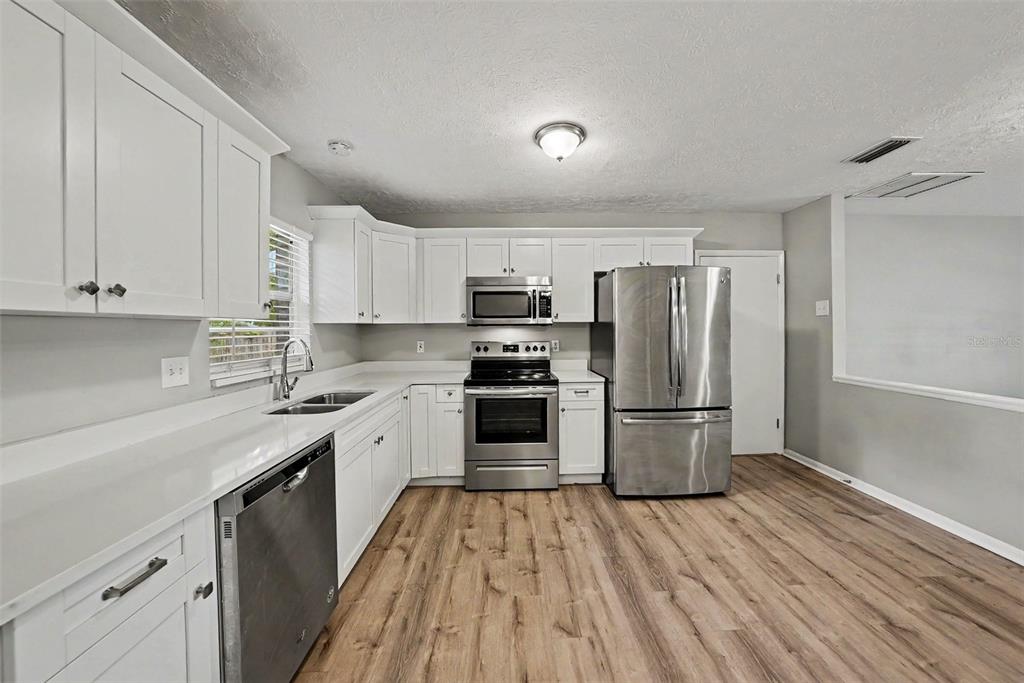 A kitchen with white cabinets, stainless steel appliances, and light wood-look flooring — 2264 VILLAGE COURT, BRANDON, FL