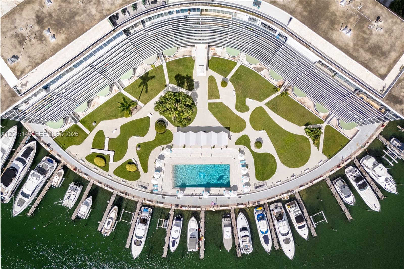 An aerial view shows a curved apartment building with a central courtyard, pool, and marina — 900 Bay Dr DS14, Miami Beach FL 33141, MIAMI BEACH, FL