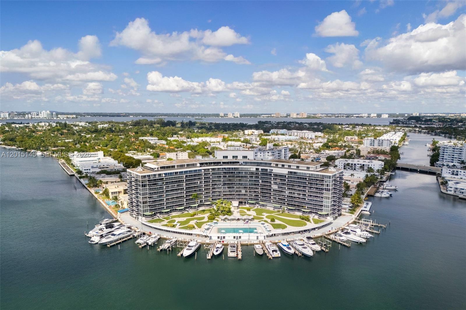 An aerial view of a curved waterfront apartment building with a pool and private marina — 900 Bay Dr DS14, Miami Beach FL 33141, MIAMI BEACH, FL