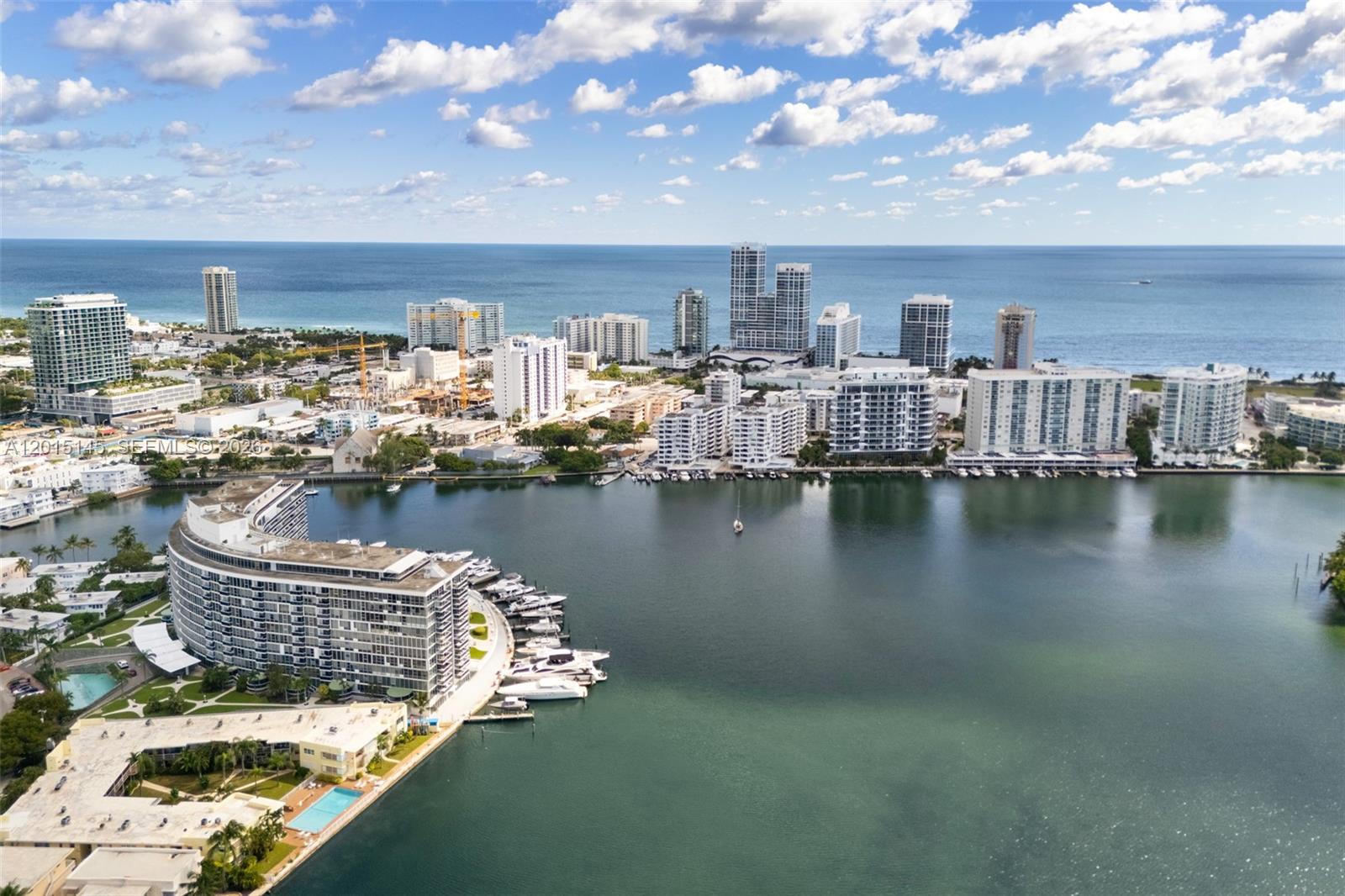 An aerial view shows a curved waterfront apartment building with a marina and city skyline — 900 Bay Dr DS14, Miami Beach FL 33141, MIAMI BEACH, FL
