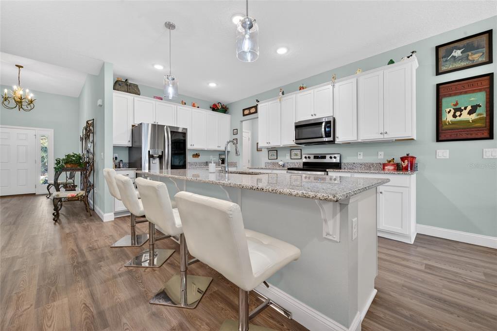 A kitchen features white cabinets, granite countertops, a central island with bar stools, and flooring — 17 WHITE HAVEN LANE, PALM COAST, FL