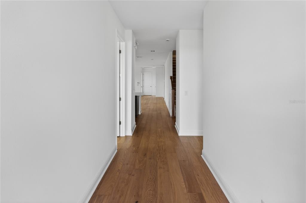 A long, narrow hallway features light wood flooring and white walls leading toward a doorway — 2926 SAILHOUSE DRIVE, ST CLOUD, FL