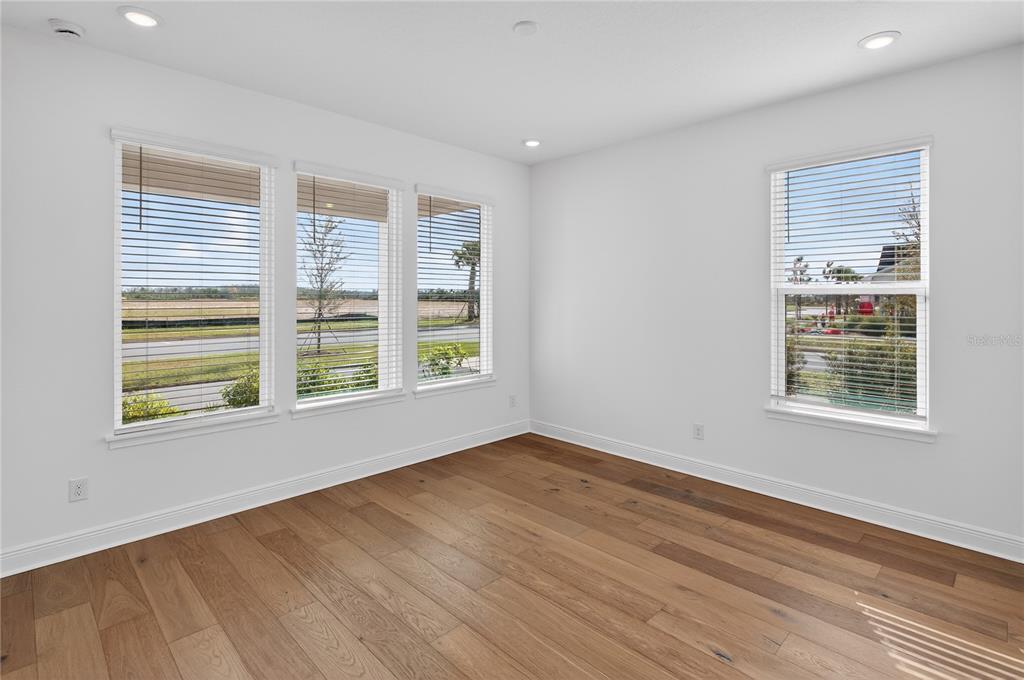 An empty room with white walls, light wood flooring, and four large windows with blinds — 2926 SAILHOUSE DRIVE, ST CLOUD, FL