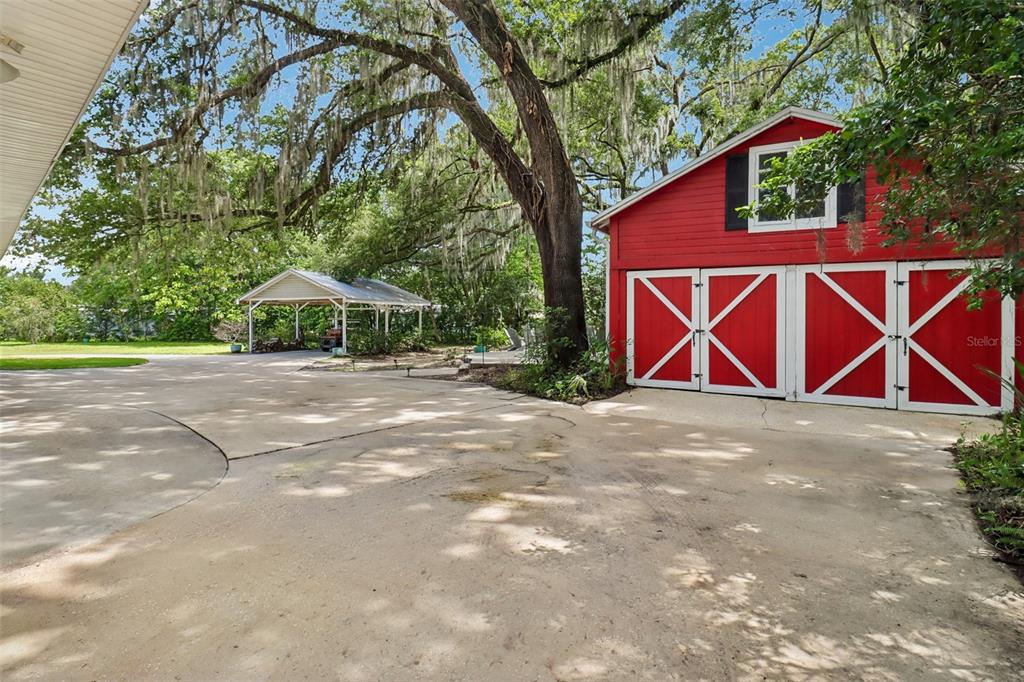 A red barn-style garage sits on a concrete driveway next to a covered carport — 649 GLENWAY DRIVE, SANFORD, FL
