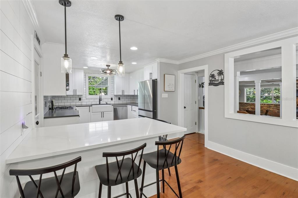 A kitchen features white cabinets, a quartz island with bar stools, and hardwood flooring — 649 GLENWAY DRIVE, SANFORD, FL