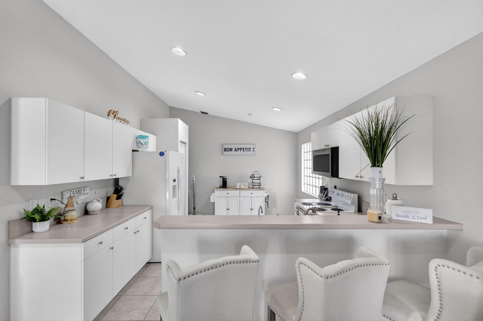 A kitchen features white cabinets, light countertops, a breakfast bar with chairs, and recessed lighting — 7207 Modena Drive, Boynton Beach FL 33437, BOYNTON BEACH, FL