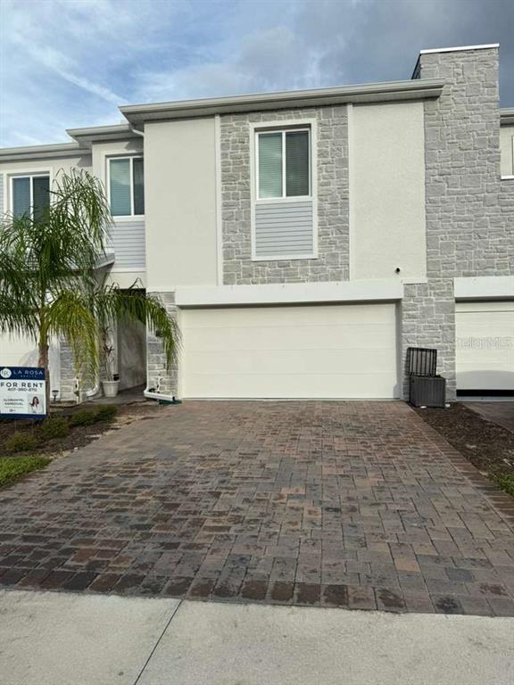 A two-story townhouse exterior features a paved driveway, a two-car garage, and stone accents — 232 NINE IRON DRIVE, DAVENPORT, FL