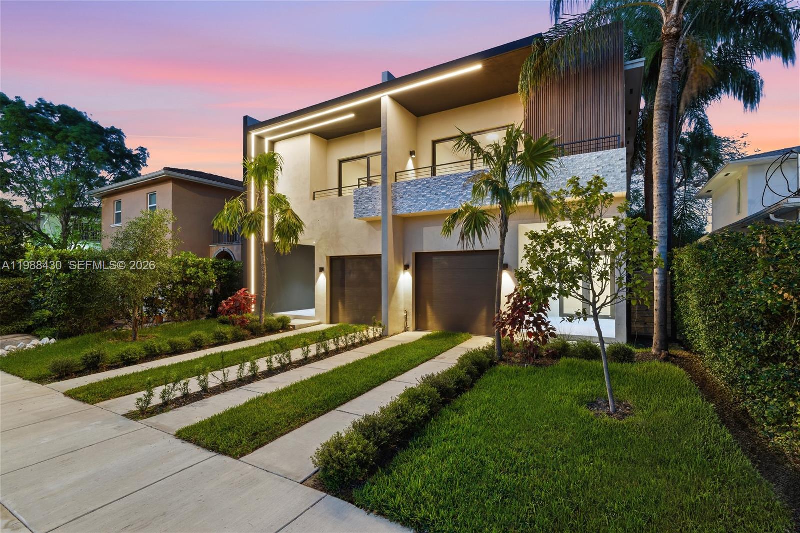 A modern two-story duplex features two garages, stone accents, and integrated exterior lighting at dusk — 2925 SW 36th Ave, Miami FL 33133, MIAMI, FL