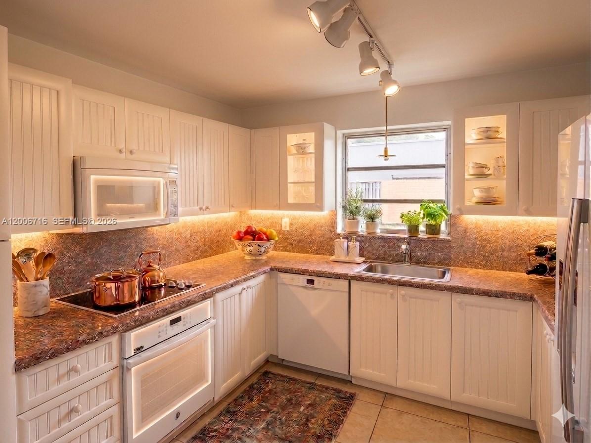 A kitchen features white cabinetry, a patterned backsplash, stainless steel appliances, and under-cabinet lighting — 3831 E 10th Ave, Hialeah FL 33013, HIALEAH, FL