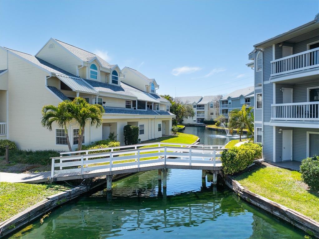 A white wooden footbridge crosses a canal between two multi-story apartment buildings — 6931 STONES THROW CIRCLE N UNIT 5302, ST PETERSBURG, FL