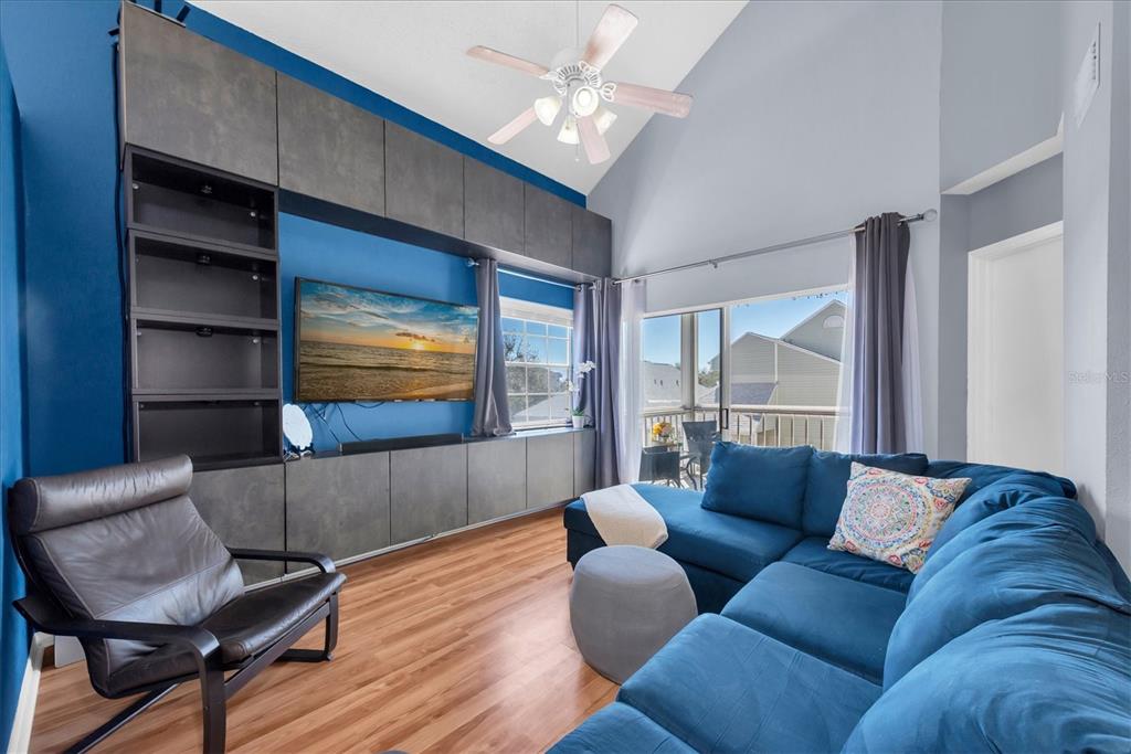 A living room features a blue accent wall, built-in gray cabinetry, a sectional sofa, and wood flooring — 6931 STONES THROW CIRCLE N UNIT 5302, ST PETERSBURG, FL