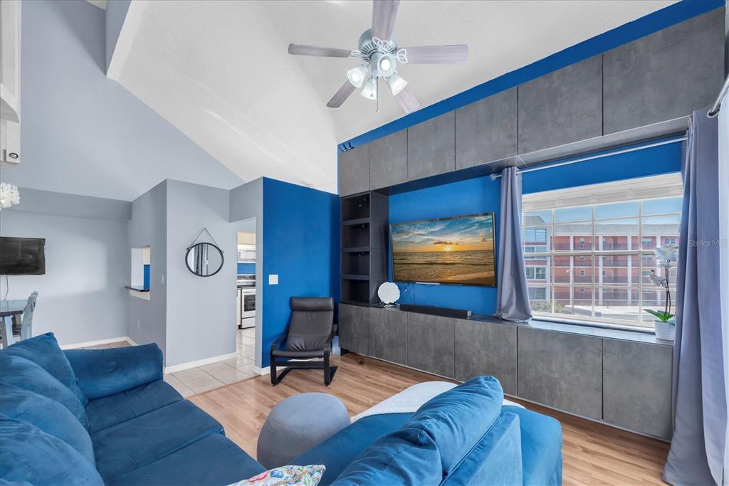 A living room features a blue sofa, a vaulted ceiling, and a grey media wall — 6931 STONES THROW CIRCLE N UNIT 5302, ST PETERSBURG, FL