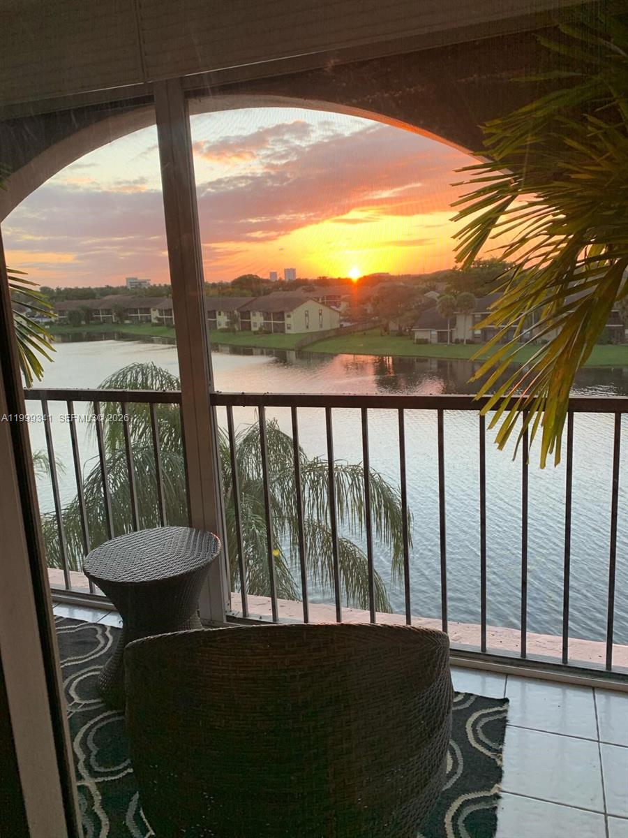 A balcony with wicker furniture overlooks a lake and residential buildings at sunset — 4025 N Nob Hill Rd # 508, Sunrise FL 33351, SUNRISE, FL