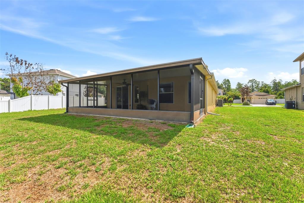 A rear view of a house featuring a large screened-in patio and a grassy backyard — 9847 EDMONTON DRIVE, LAND O LAKES, FL