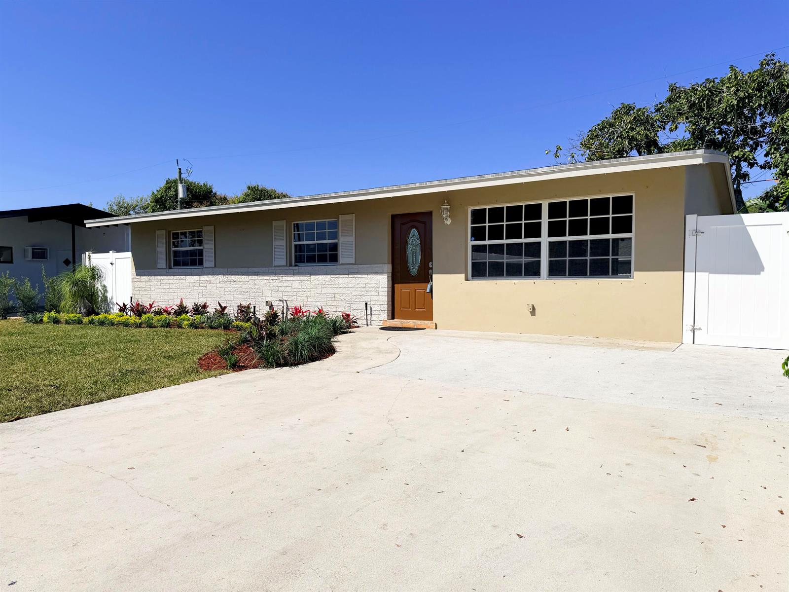 A single-story house with a tan exterior, stone facade, brown front door, and concrete driveway — 63 Andros Road, Palm Springs FL 33461, PALM SPRINGS, FL