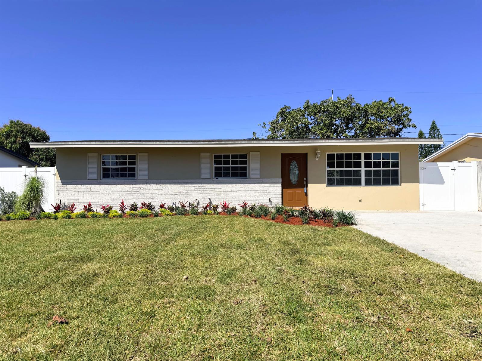 A single-story house with a tan exterior, white brick accents, and a front lawn — 63 Andros Road, Palm Springs FL 33461, PALM SPRINGS, FL