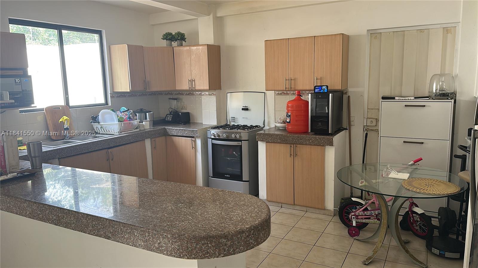A kitchen features light wood cabinets, granite countertops, a gas stove, and a glass table — La Serena Mzna 4 Villa 11 Calle 3era, G, G