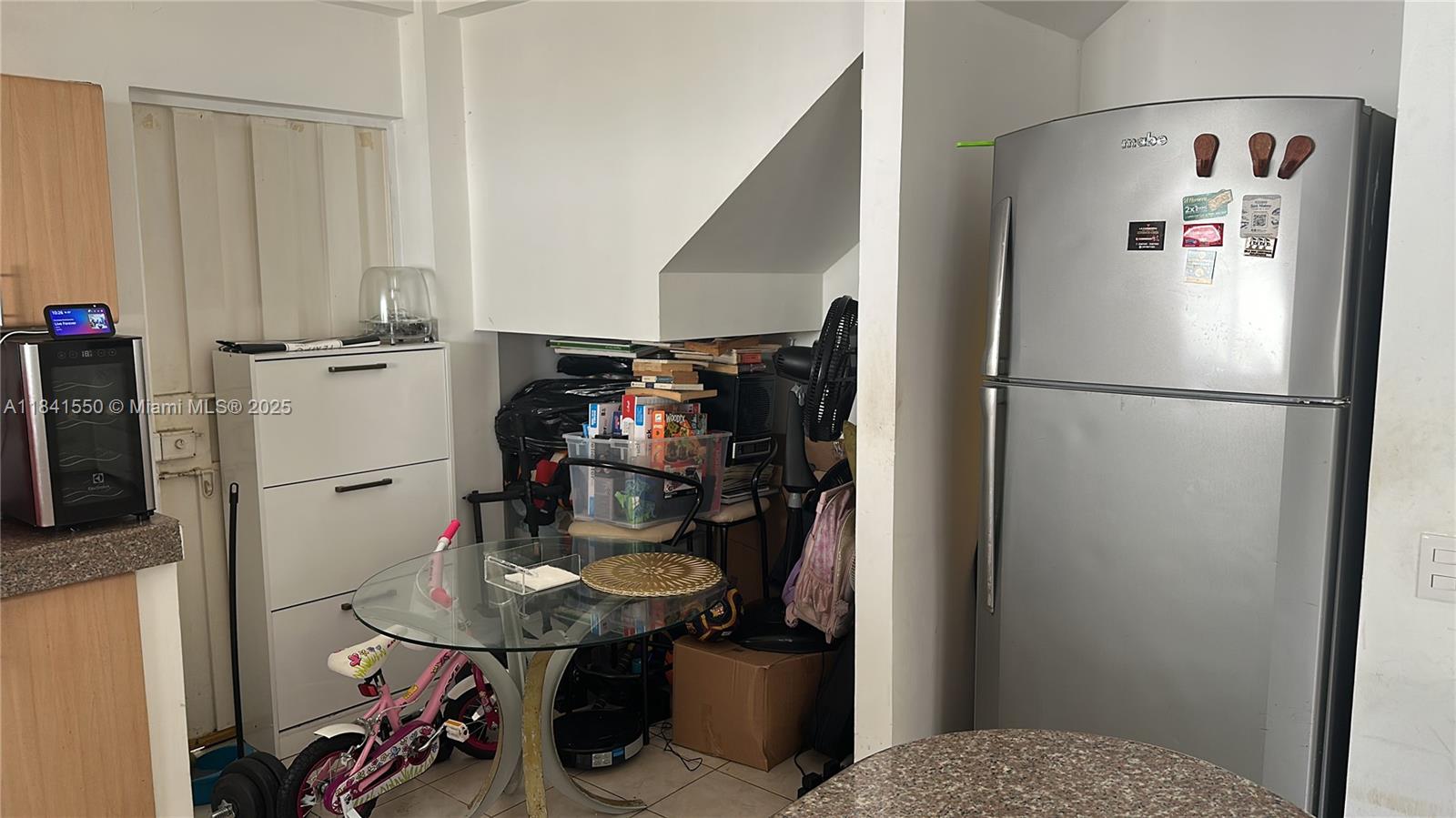 A kitchen area features a stainless steel refrigerator, a glass table, and a small bicycle — La Serena Mzna 4 Villa 11 Calle 3era, G, G