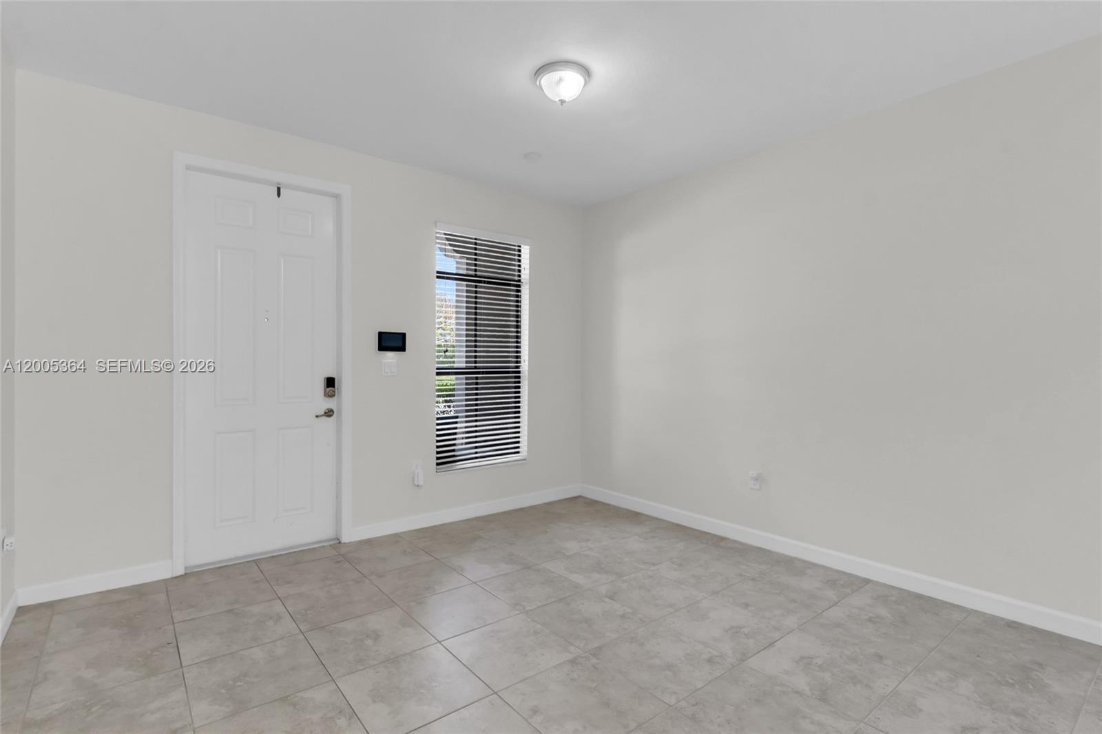 An empty room features light gray tile flooring, white walls, a white door, and blinds — 11738 SW 238th St, Homestead FL 33032, HOMESTEAD, FL