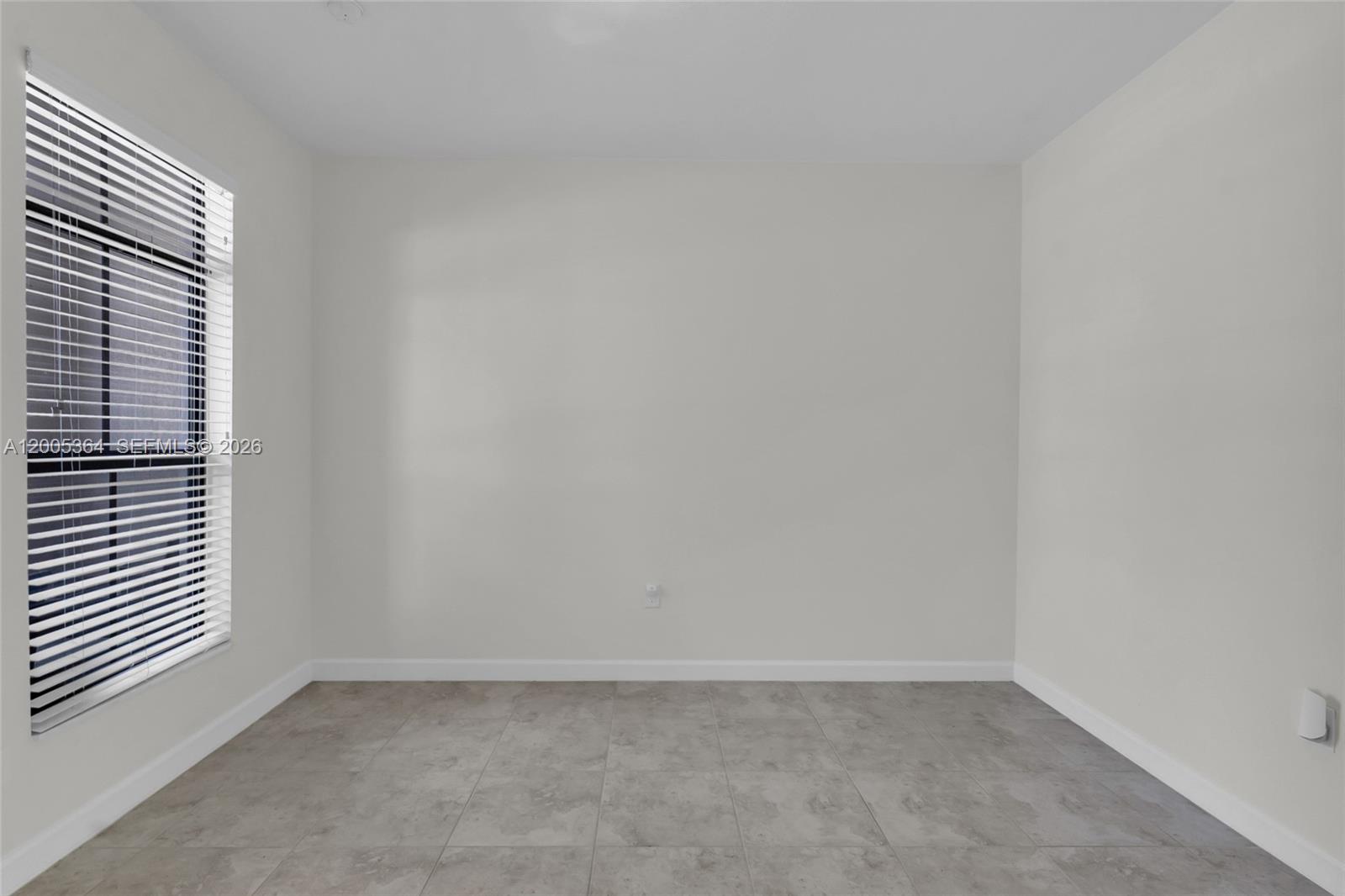 An empty room features light gray walls, large floor tiles, and a window with blinds — 11738 SW 238th St, Homestead FL 33032, HOMESTEAD, FL