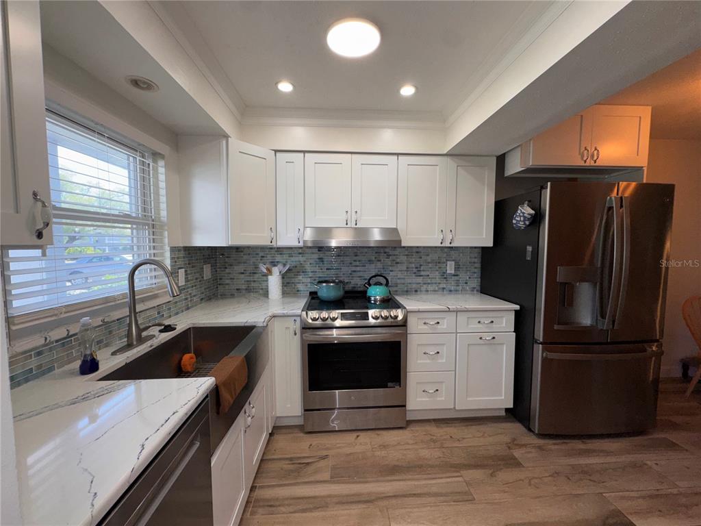 A kitchen features white cabinets, stainless steel appliances, a farmhouse sink, and a tiled backsplash — 202 46TH TERRACE W UNIT #207, BRADENTON, FL