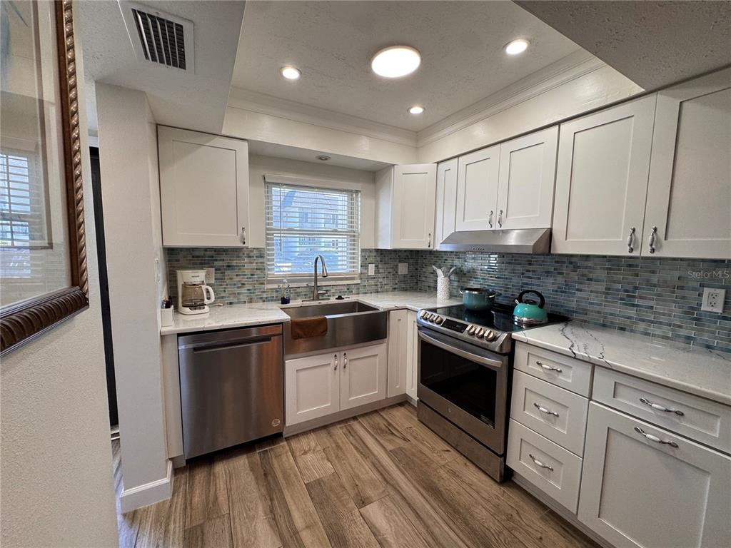 A kitchen features white cabinets, stainless steel appliances, a farmhouse sink, and blue tile backsplash — 202 46TH TERRACE W UNIT #207, BRADENTON, FL