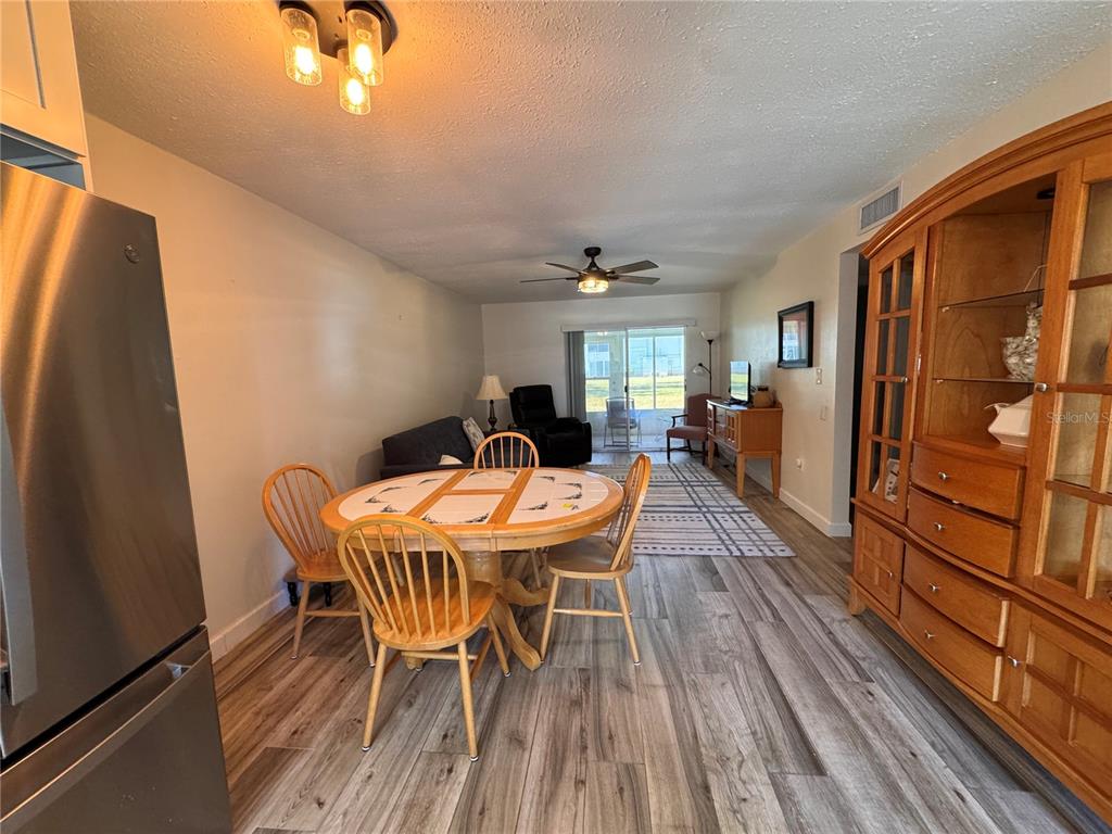A dining area with a wooden table and chairs leads into a living room space — 202 46TH TERRACE W UNIT #207, BRADENTON, FL