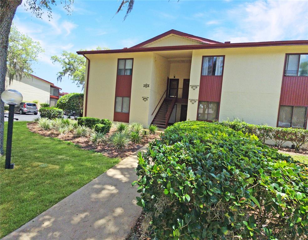A two-story apartment building exterior features a central staircase, tan stucco walls, and landscaping — 648 MIDWAY DRIVE UNIT B, OCALA, FL