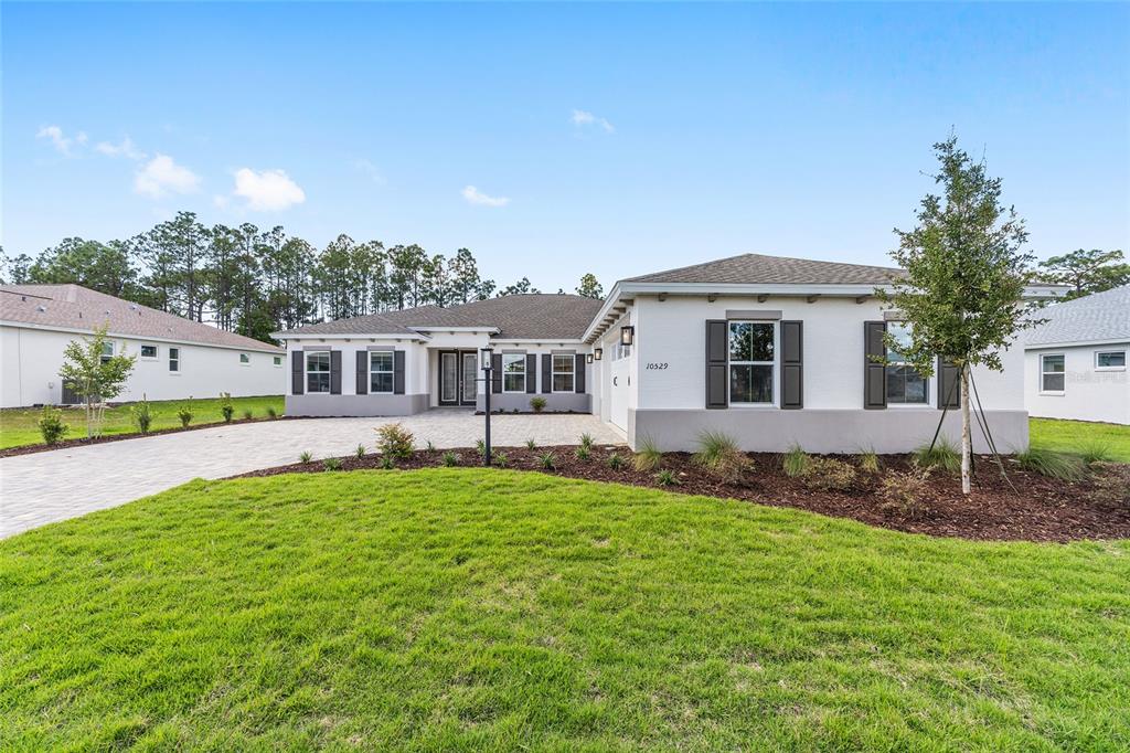 A single-story house with a white stucco exterior, dark shutters, and a paved driveway — 10529 SW 96TH LANE ROAD, OCALA, FL