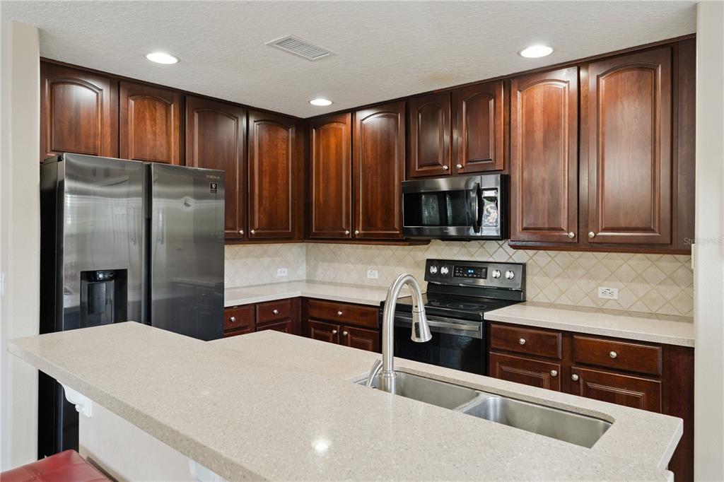 A kitchen features dark wood cabinets, stainless steel appliances, and a light-colored stone countertop — 3527 CARUSO PLACE, OVIEDO, FL