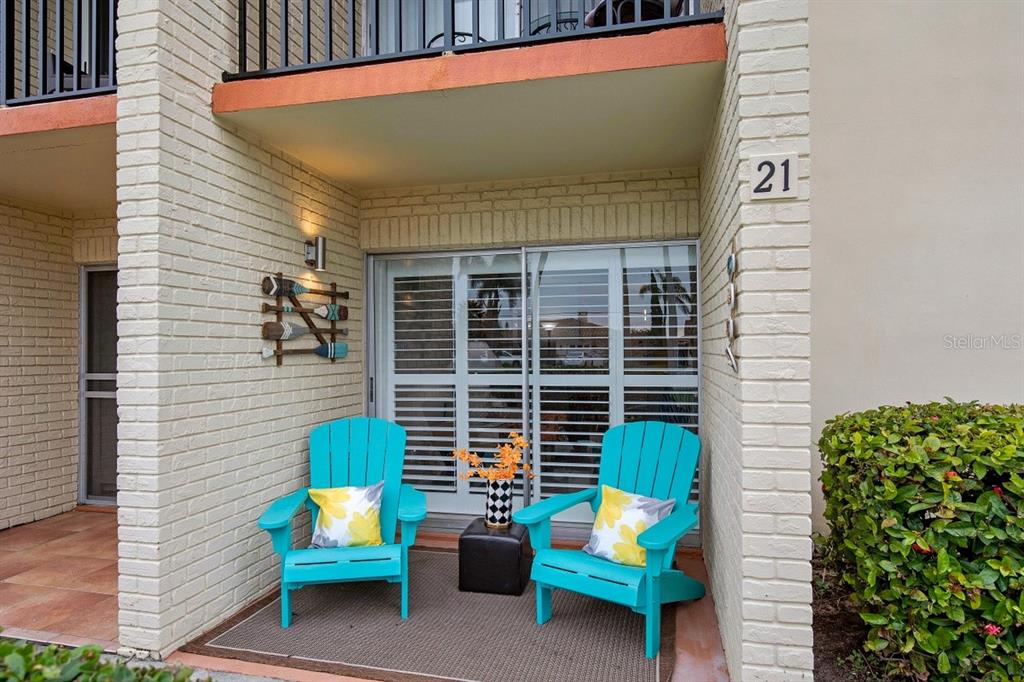 A patio features two turquoise Adirondack chairs, a small table, and decorative oars on the wall — 10365 PARADISE BOULEVARD UNIT 21, TREASURE ISLAND, FL
