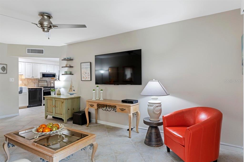 A living room features a wall-mounted television, a red armchair, and tile flooring — 10365 PARADISE BOULEVARD UNIT 21, TREASURE ISLAND, FL