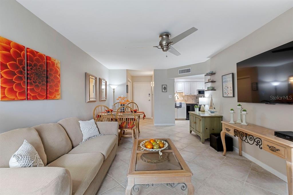 A living room with a beige sofa, coffee table, dining area, and wall-mounted television — 10365 PARADISE BOULEVARD UNIT 21, TREASURE ISLAND, FL