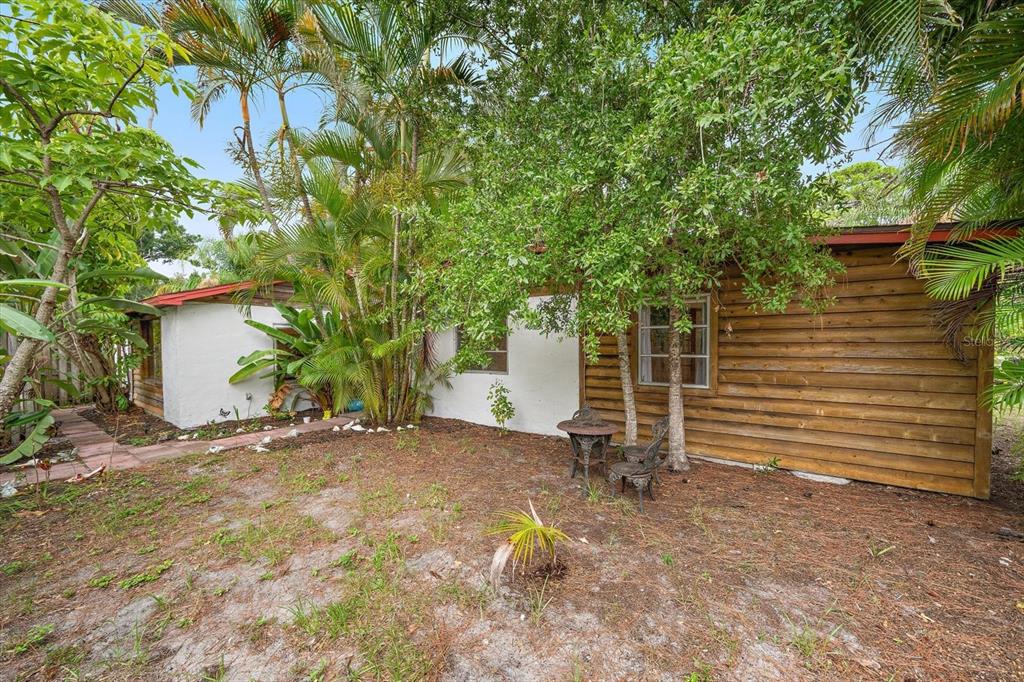 A single-story house with a white stucco and wood-paneled exterior sits in a wooded yard — 4102 ROYAL PALM AVENUE, SARASOTA, FL