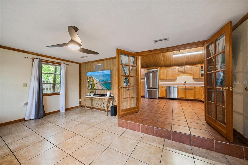 A living room with tile floors and wood paneling leads to a kitchen via French doors — 4102 ROYAL PALM AVENUE, SARASOTA, FL