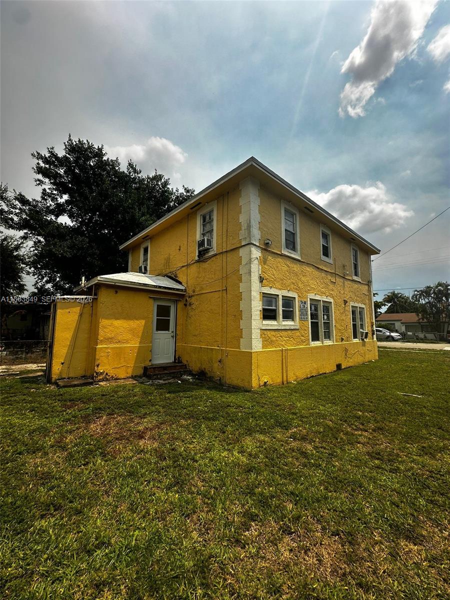 A two-story yellow house with white corner accents stands on a grassy lot — 1925 NW 56th St, Miami FL 33142, MIAMI, FL