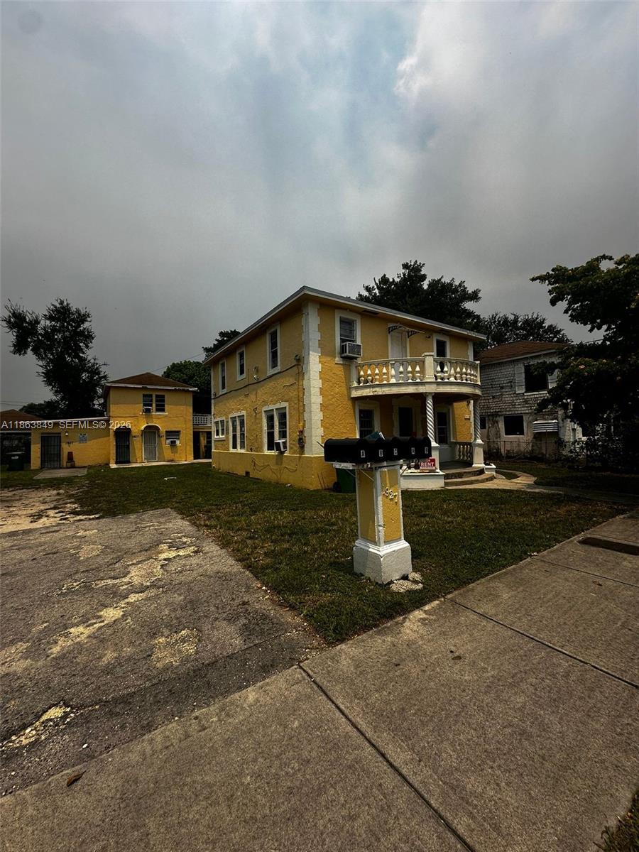 A yellow two-story house with a balcony and a detached structure on a grassy lot — 1925 NW 56th St, Miami FL 33142, MIAMI, FL