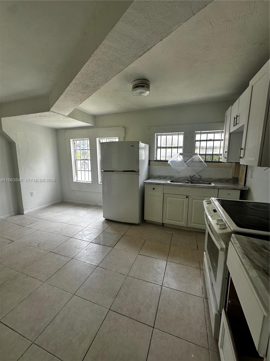 This kitchen features white cabinets, a white refrigerator, a stove, and light-colored tile flooring — 1925 NW 56th St, Miami FL 33142, MIAMI, FL