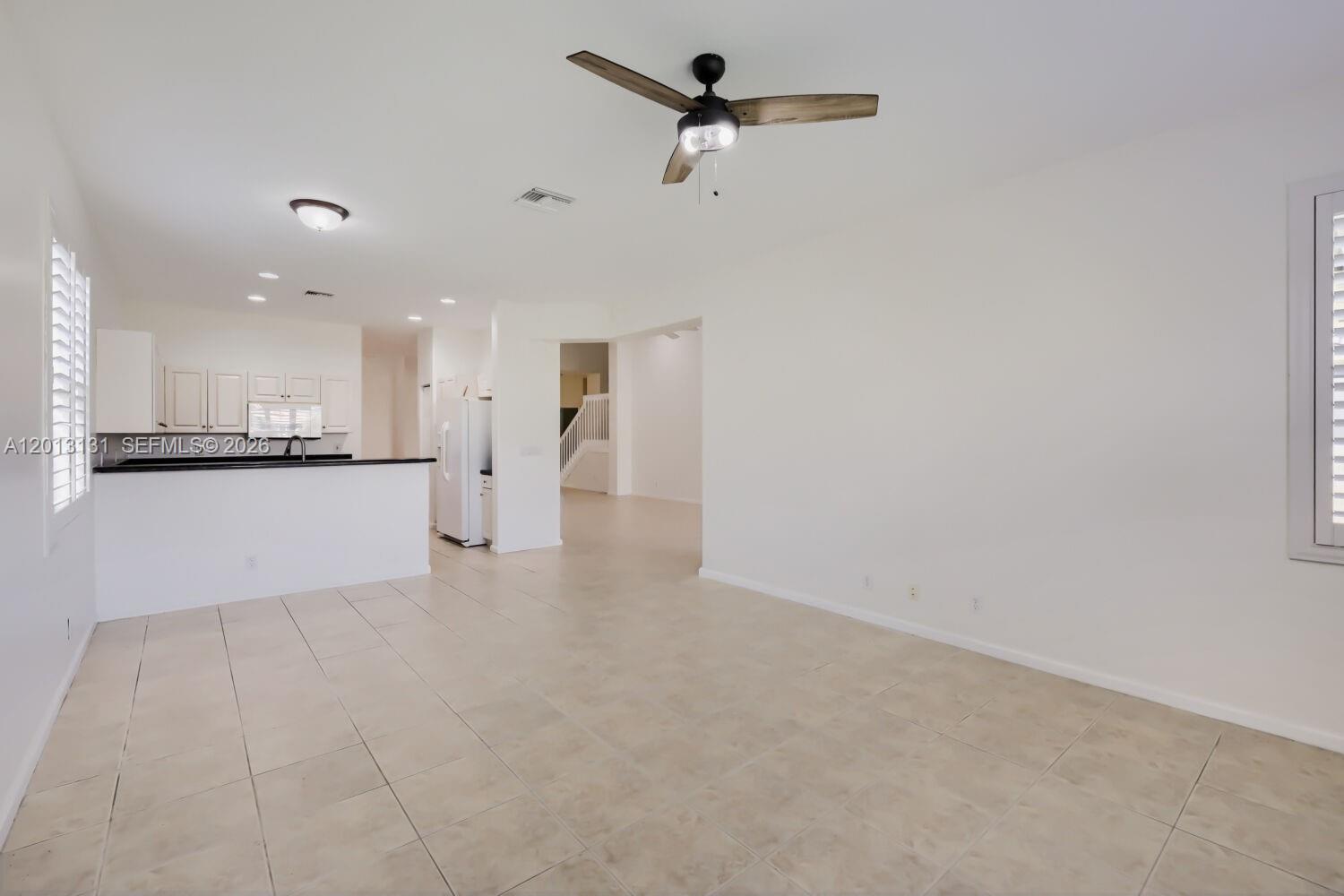 An open-concept living area features light tile flooring, white walls, and a ceiling fan — 117 Palm Cir, Atlantis FL 33462, ATLANTIS, FL