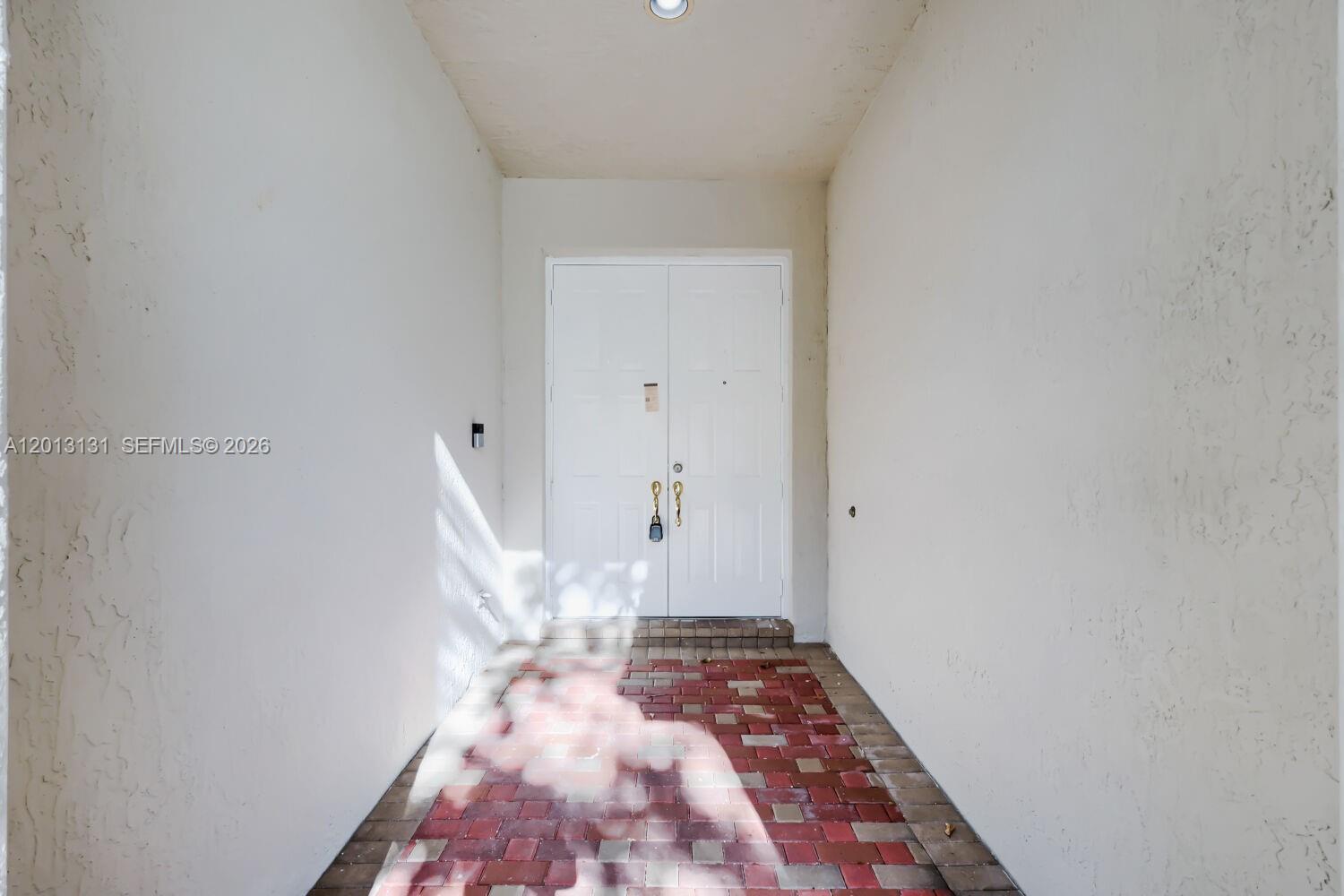 A recessed entryway features white double doors, a brick paver floor, and textured walls — 117 Palm Cir, Atlantis FL 33462, ATLANTIS, FL