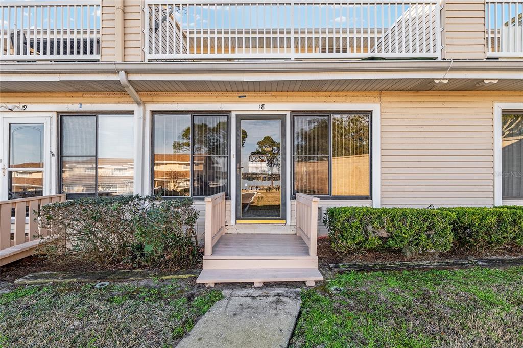 The exterior of a multi-story residential building features a small wooden porch and stairs — 11001 SE SUNSET HARBOR ROAD UNIT D18, SUMMERFIELD, FL