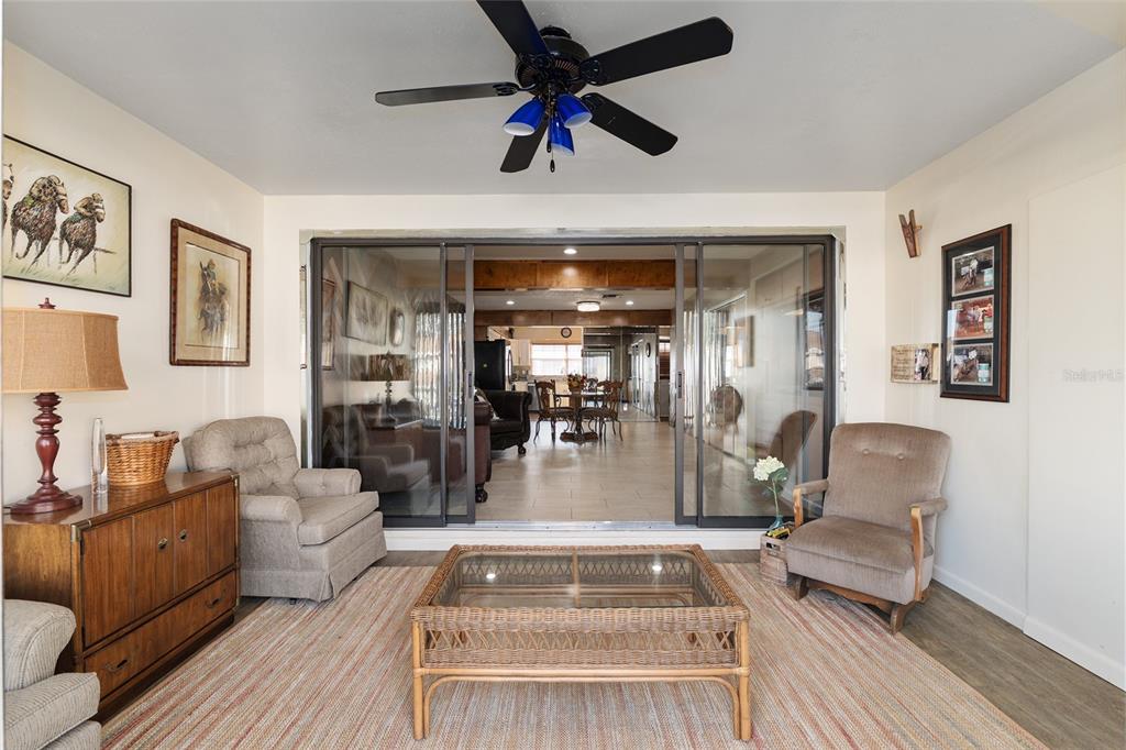 A sunroom with a ceiling fan, sliding glass doors, and two armchairs facing a coffee table — 11001 SE SUNSET HARBOR ROAD UNIT D18, SUMMERFIELD, FL