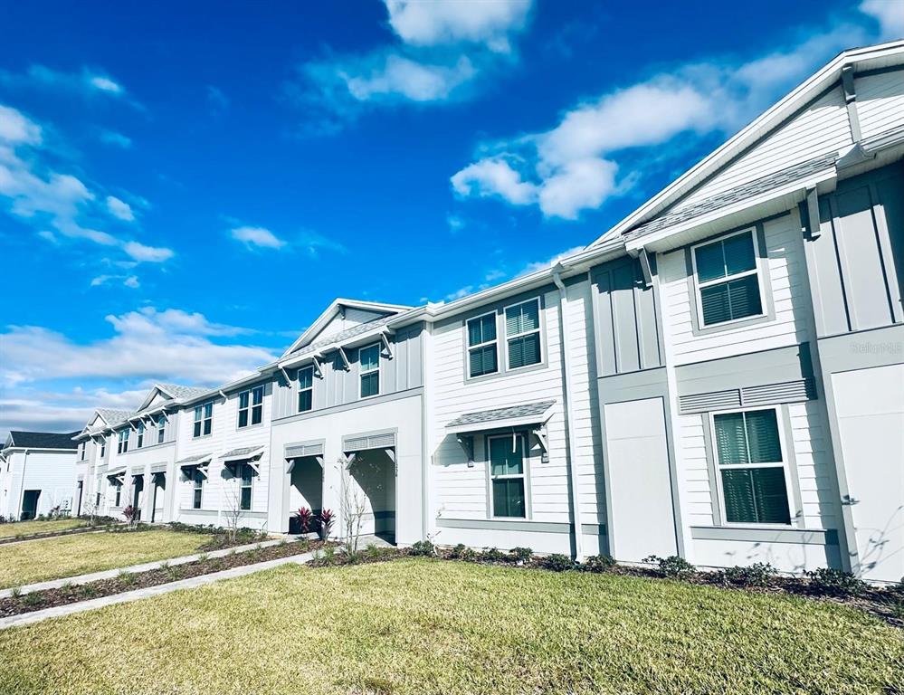 A row of modern two-story townhomes with white siding and gray trim under a blue sky — 1256 BLUE PARADISE DRIVE, CLERMONT, FL