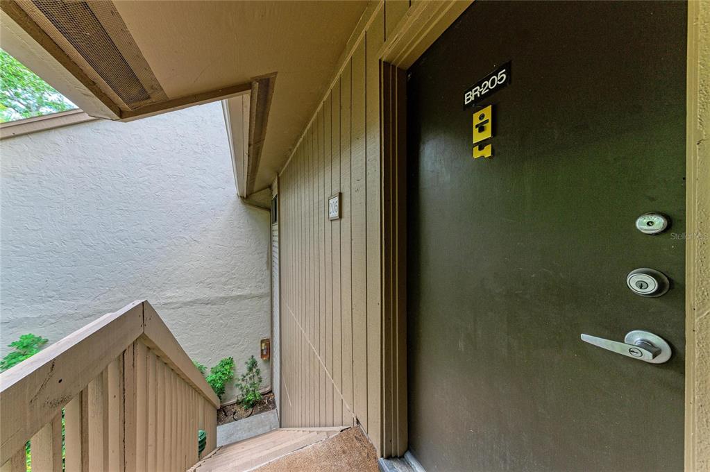 A brown exterior door labeled BR-205 is adjacent to a wooden staircase — 1709 CLOWER CREEK DRIVE UNIT 205, SARASOTA, FL