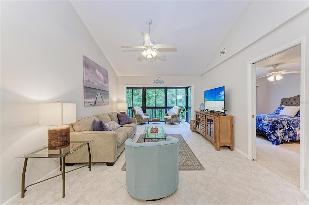 A living room with a vaulted ceiling, tile floors, and a view of a screened porch — 1709 CLOWER CREEK DRIVE UNIT 205, SARASOTA, FL