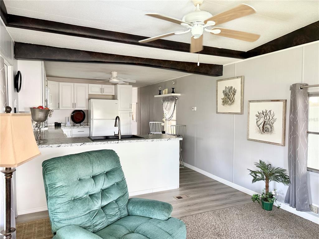 A living room with a green armchair opens to a kitchen featuring white cabinets — 34543 SWEETPEA LANE, ZEPHYRHILLS, FL