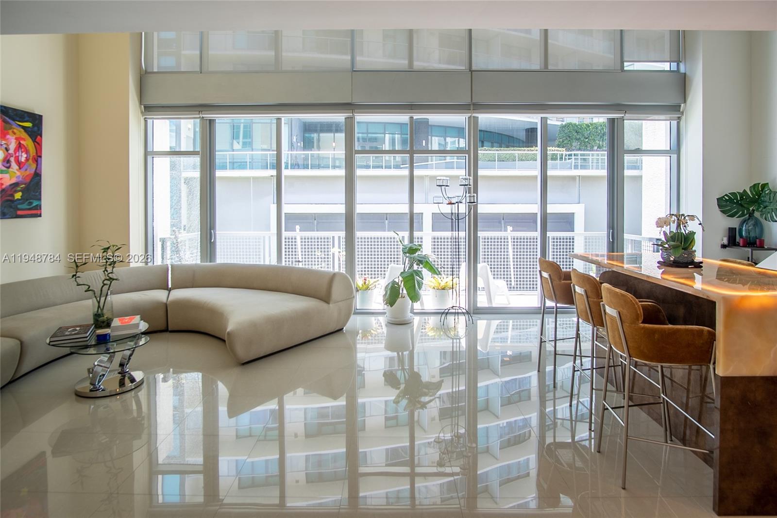 A modern living room features a curved sofa, a breakfast bar, and floor-to-ceiling windows — 3301 NE 1st Ave, Miami FL 33137, MIAMI, FL
