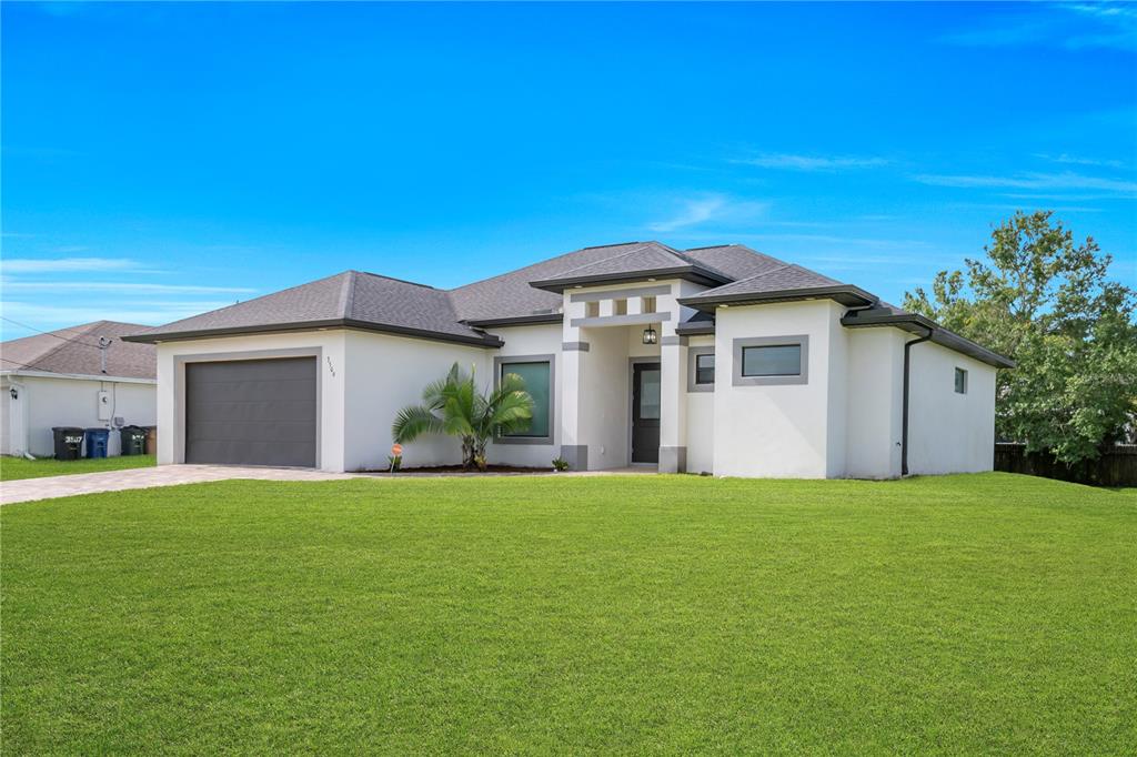 A single-story house with a white stucco exterior, a gray garage door, and a green lawn — 3509 38TH ST SW, LEHIGH ACRES, FL