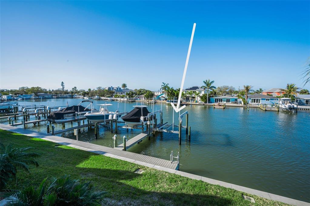 A boat lift sits in a canal next to a grassy lawn and concrete seawall — 140 MARCDALE BOULEVARD, INDIAN ROCKS BEACH, FL